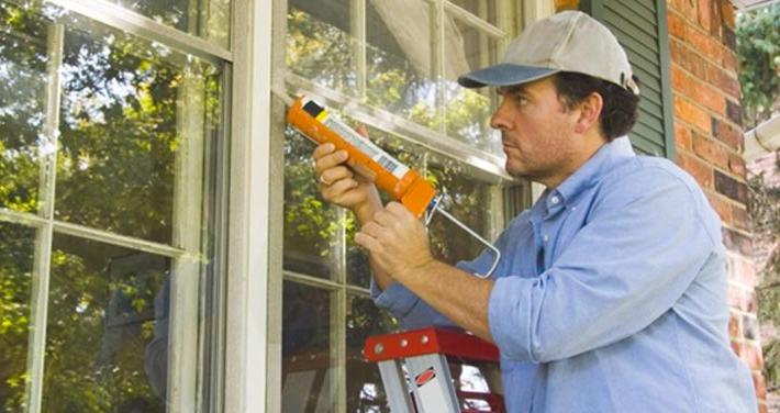 man on ladder caulking window