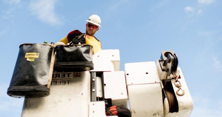 Lineworker looking down from a bucket against a blue sky